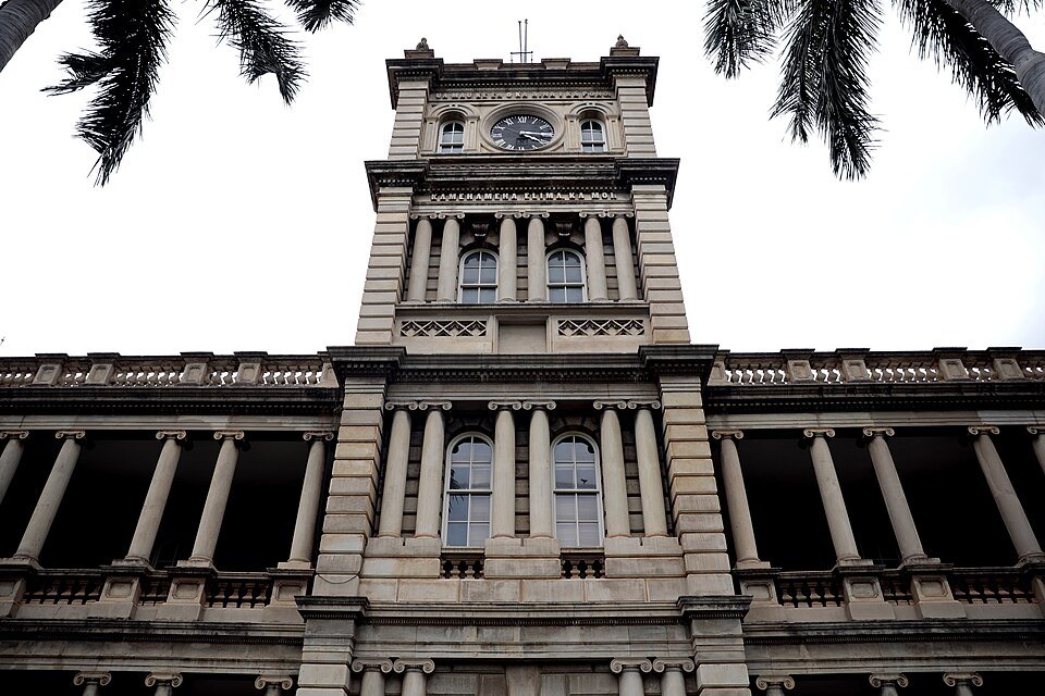 The clock tower of Aliʻiōlani Hale, seen from below between palms