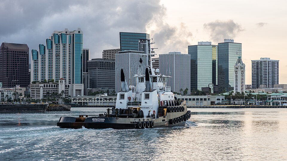 A harbor tug in front of the downtown towers, Aloha Tower at the right