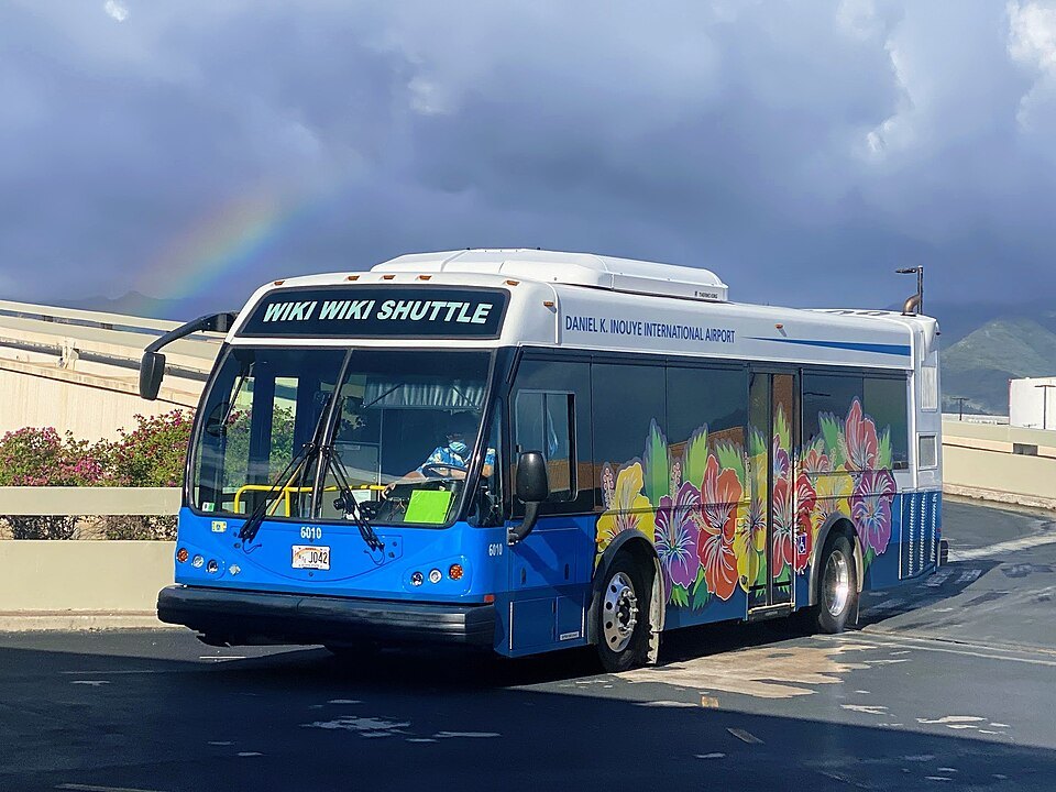A Wiki Wiki Shuttle bus painted with flowers, a rainbow over the airport