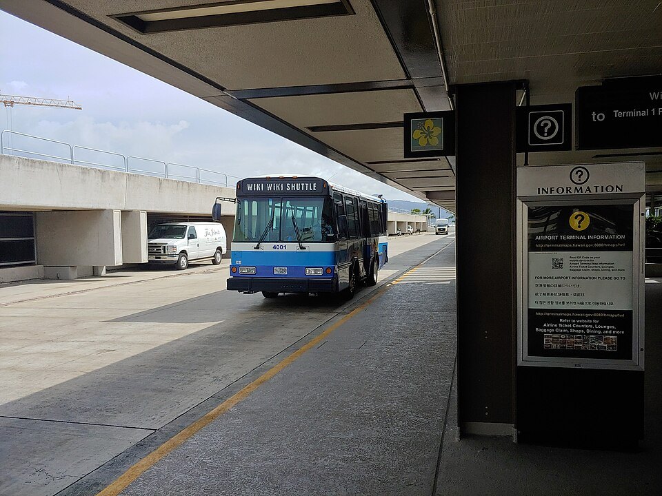 The Wiki Wiki Shuttle at a terminal stop, airport information sign beside it