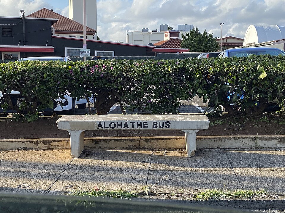 A stone bench carved ALOHA THE BUS at a bus stop